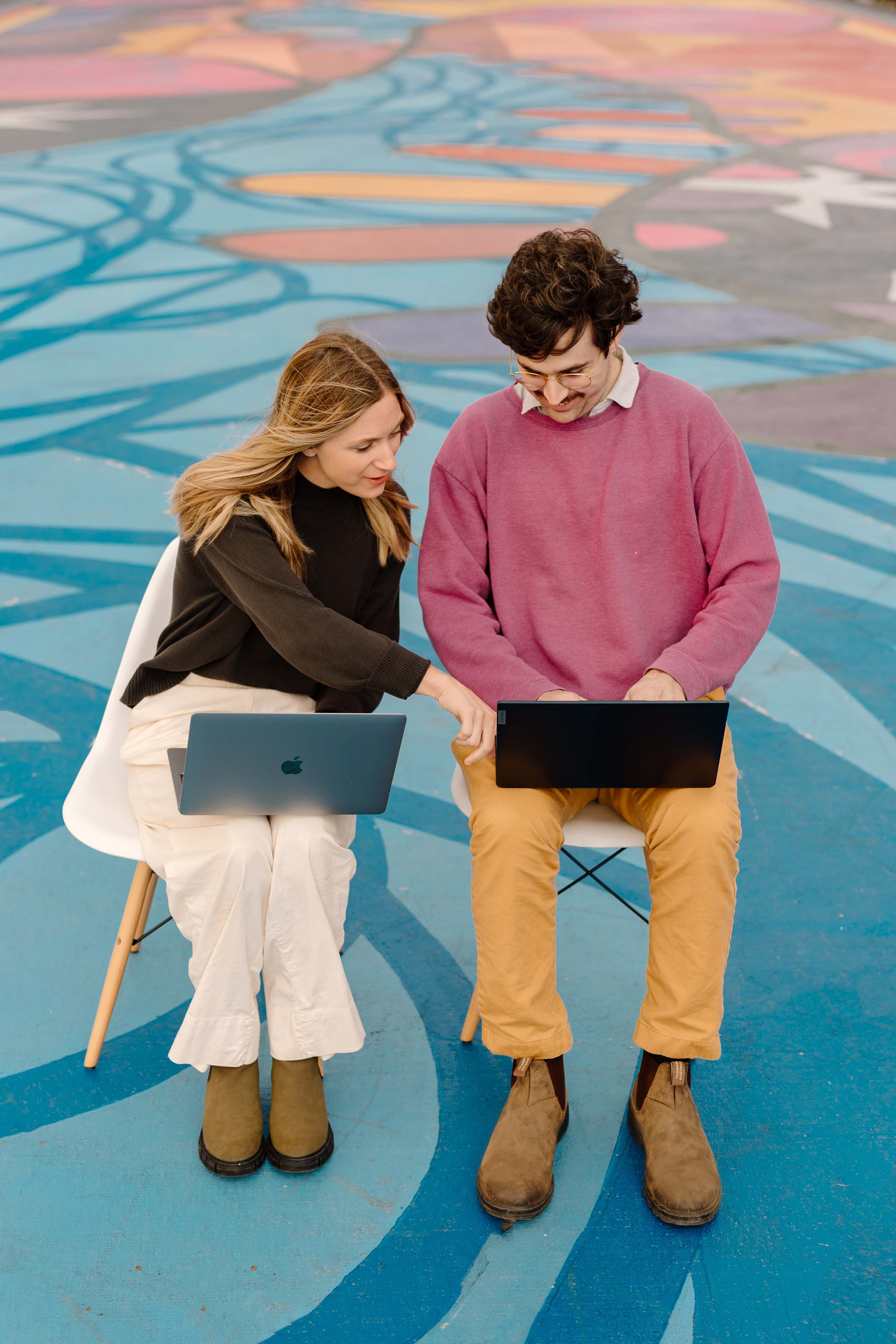 two people sitting on chairs in a colorful sitting looking at their laptops
