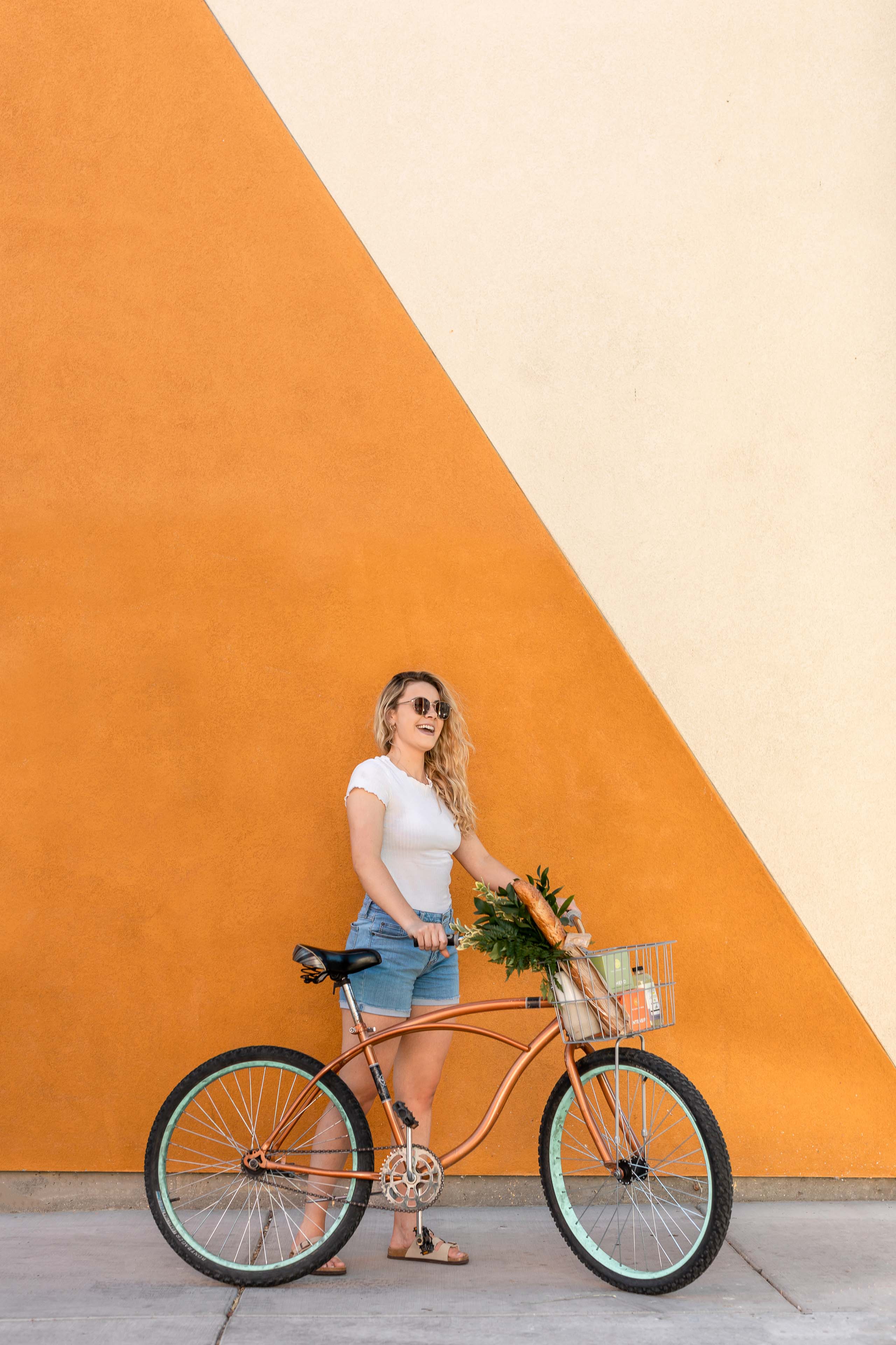 a woman standing near a bike with a colorful wall in the background