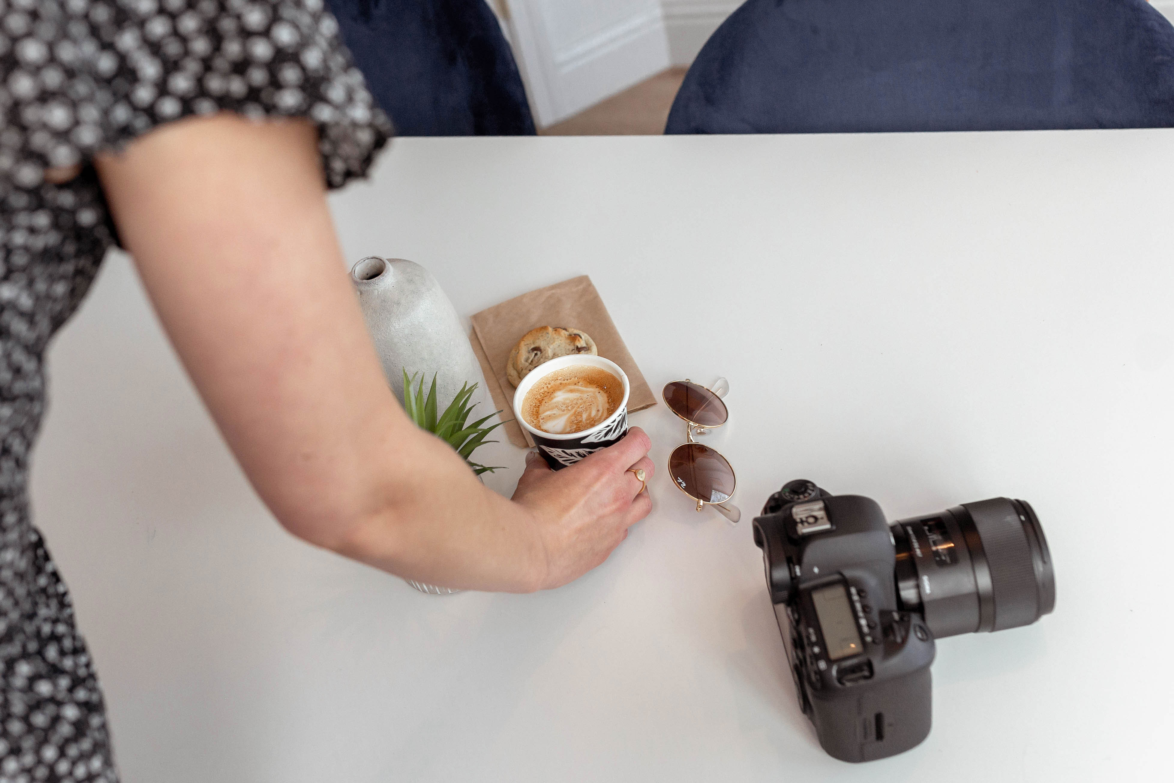 Person adjusting a coffee cup on a table with a pastery and camera on the table