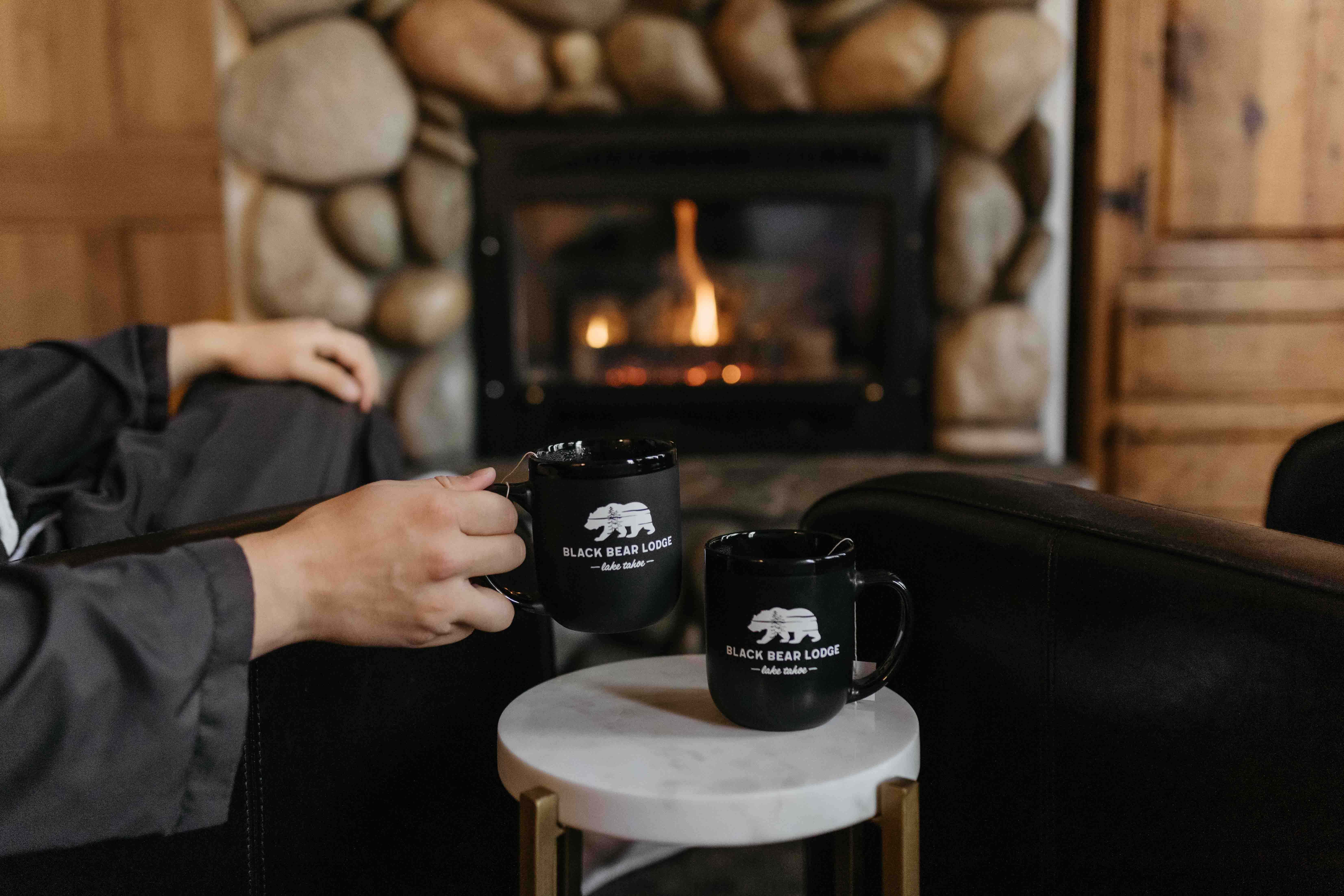Person lifting a coffee mug and fire place in the background