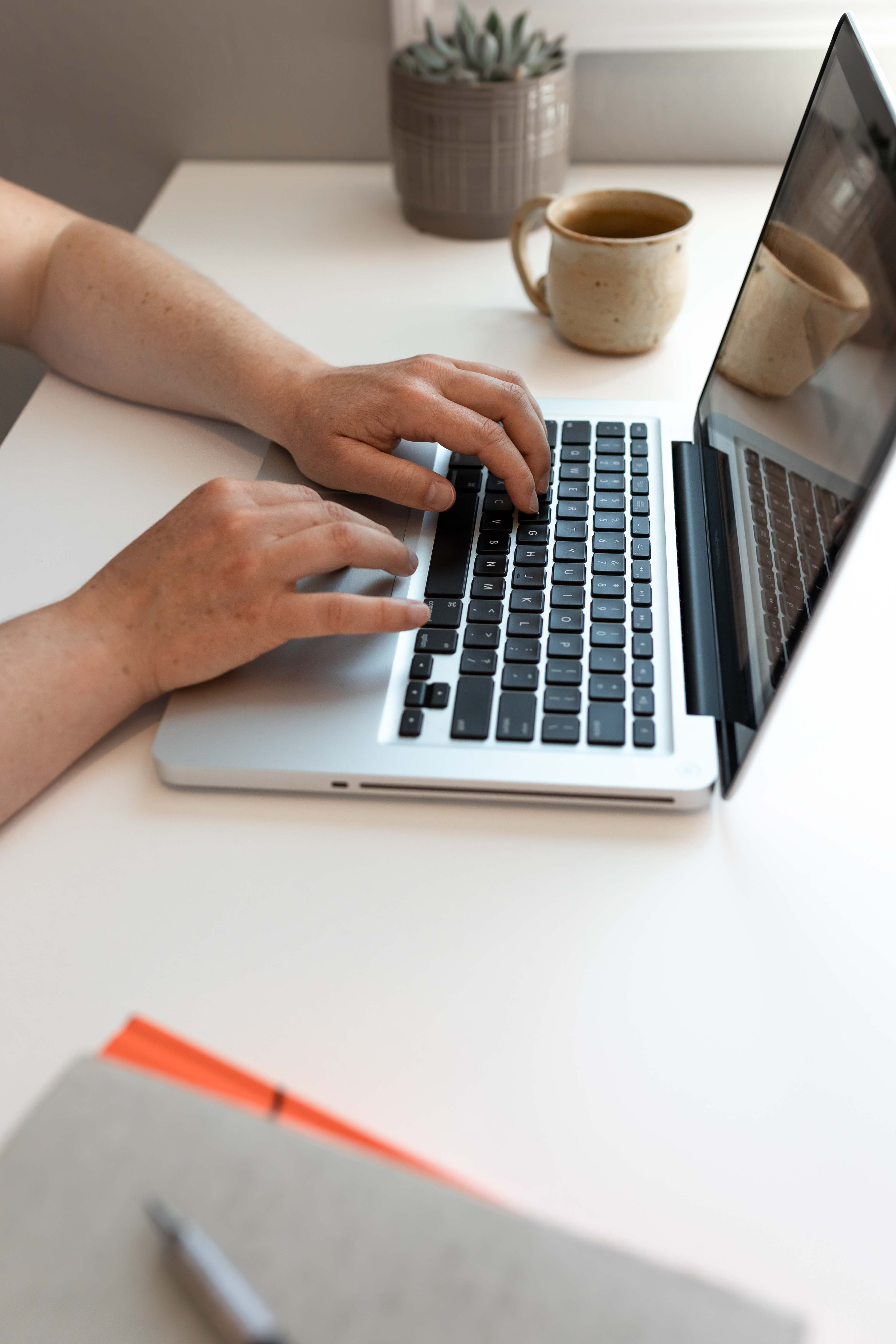Person typing on a laptop with a mug of coffee in the background