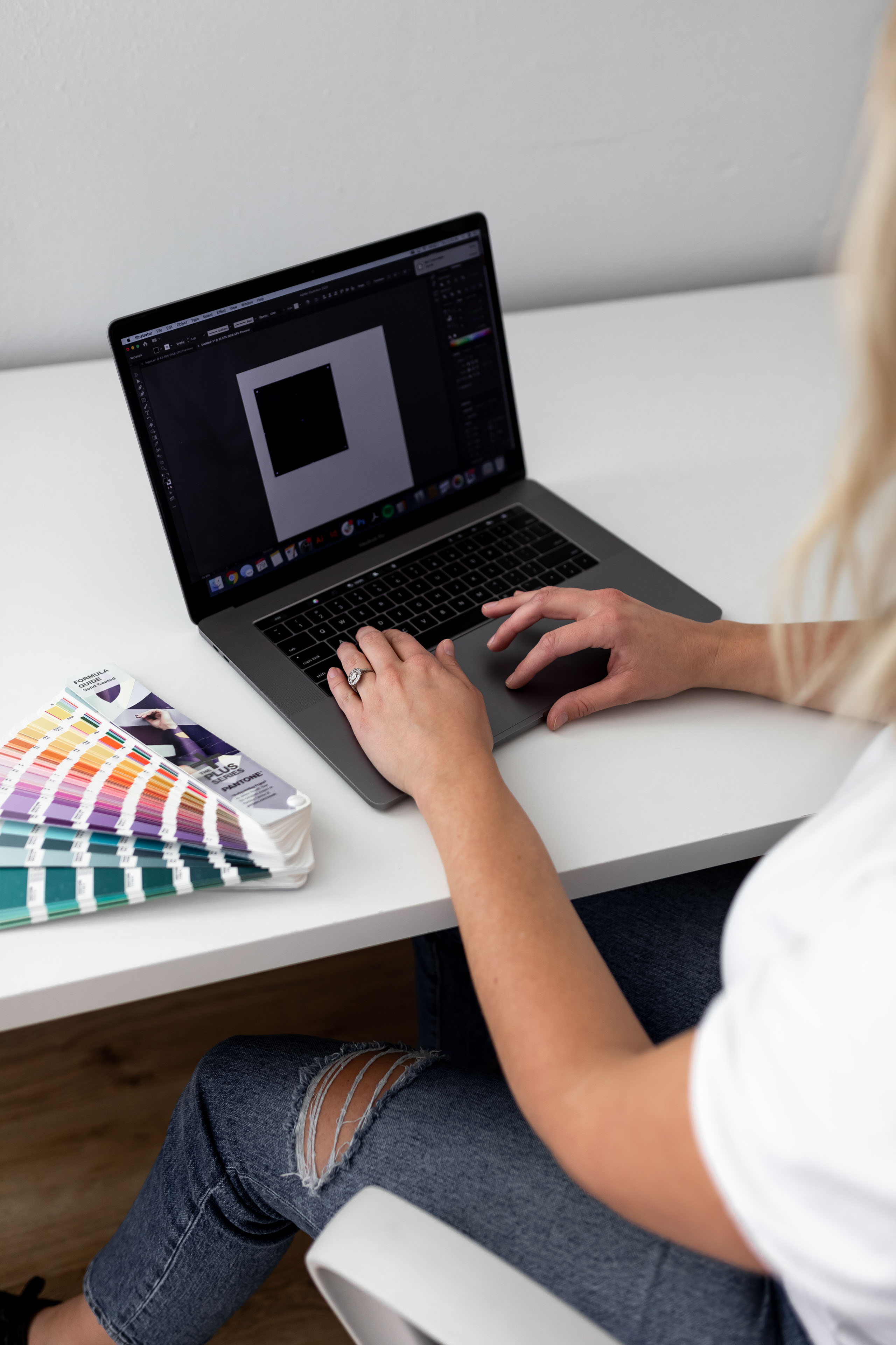 a person designing on a laptop with a colorful pantone book on the desk next to them copy