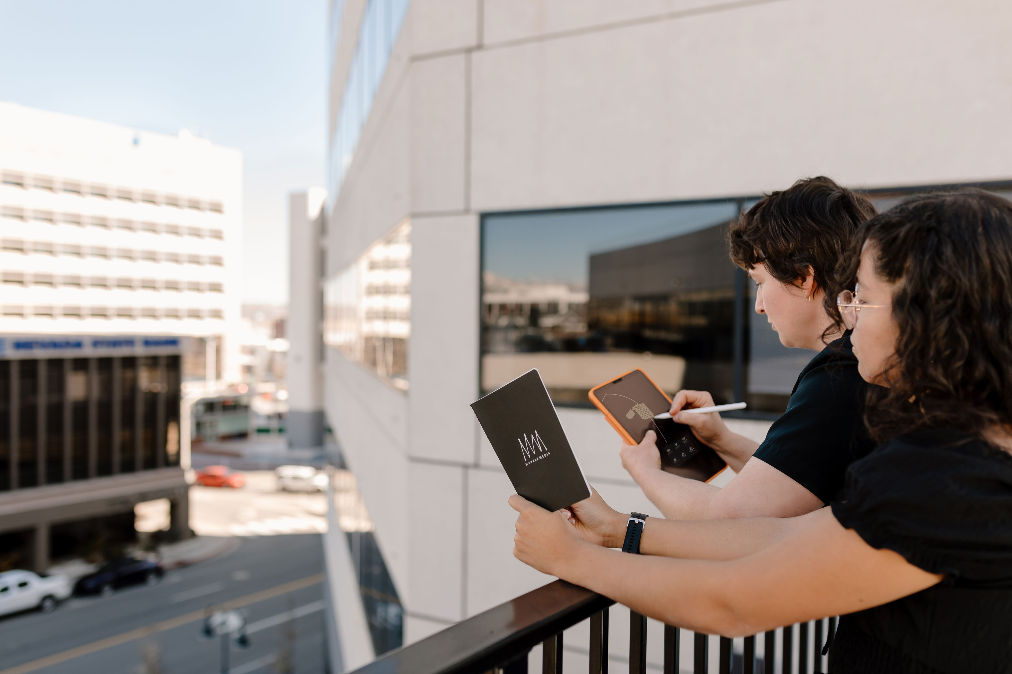 a woman holding a notebook and another sketching on an ipad