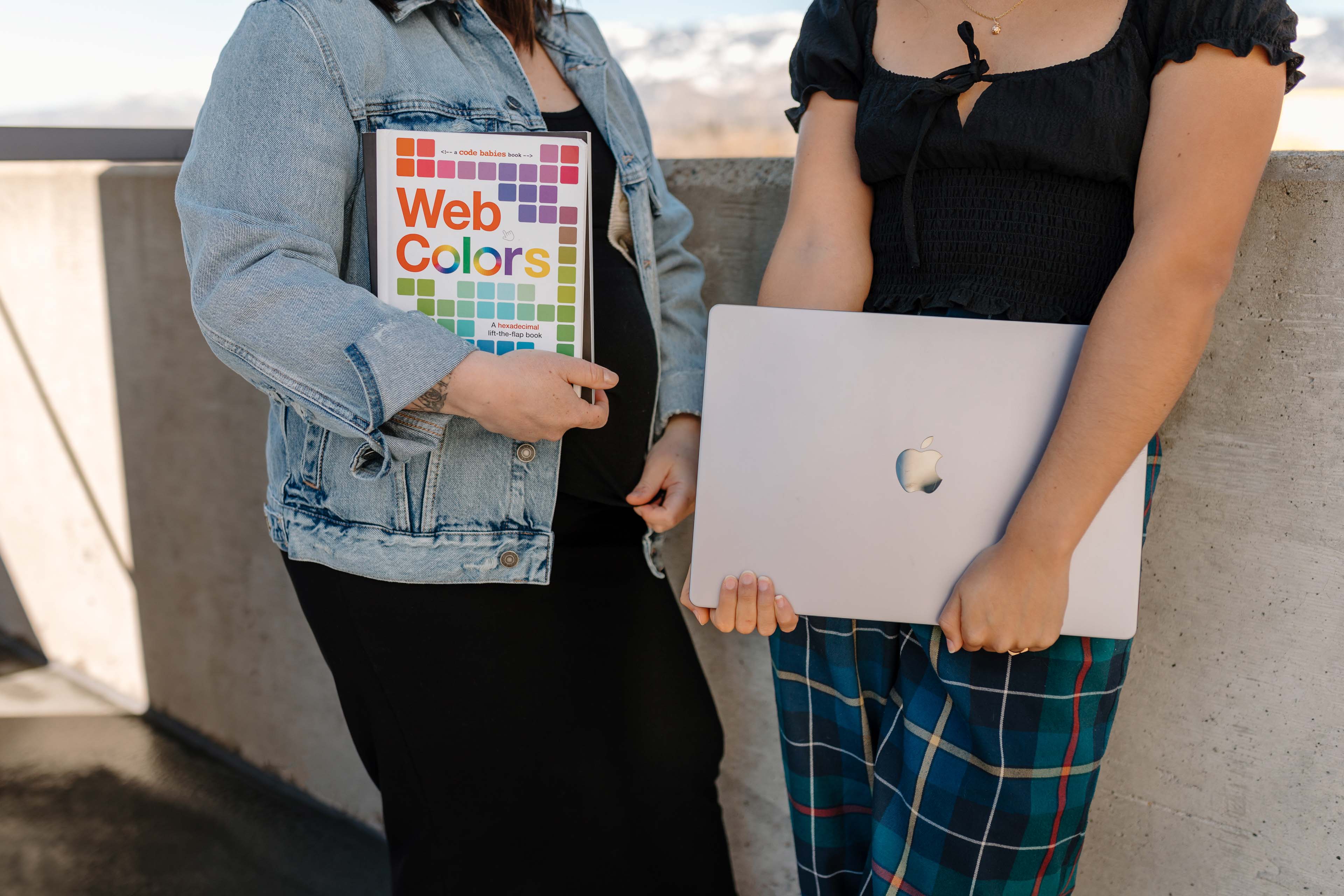 two people holding a laptop and a book about web design