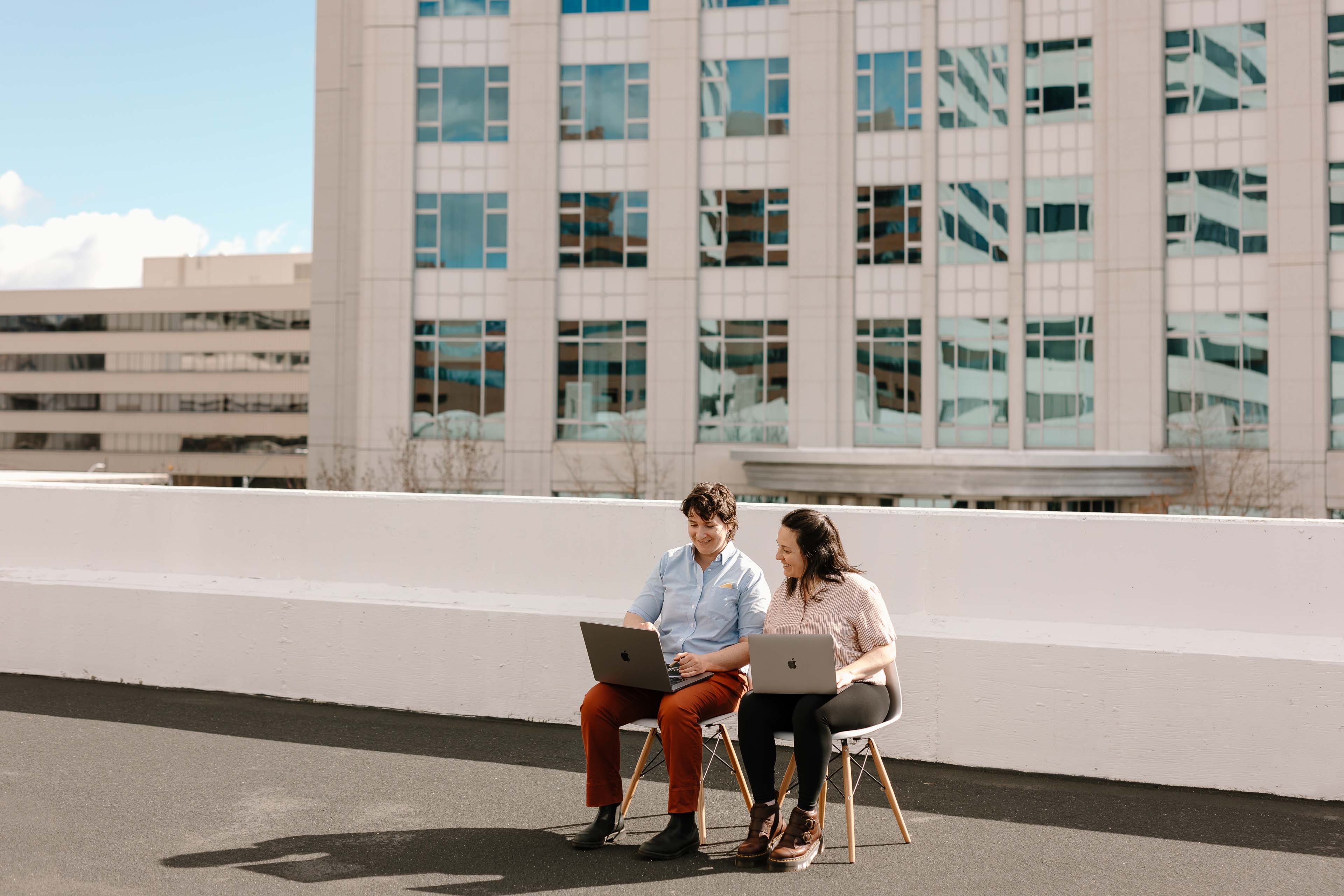 two people sitting in a city working on laptops