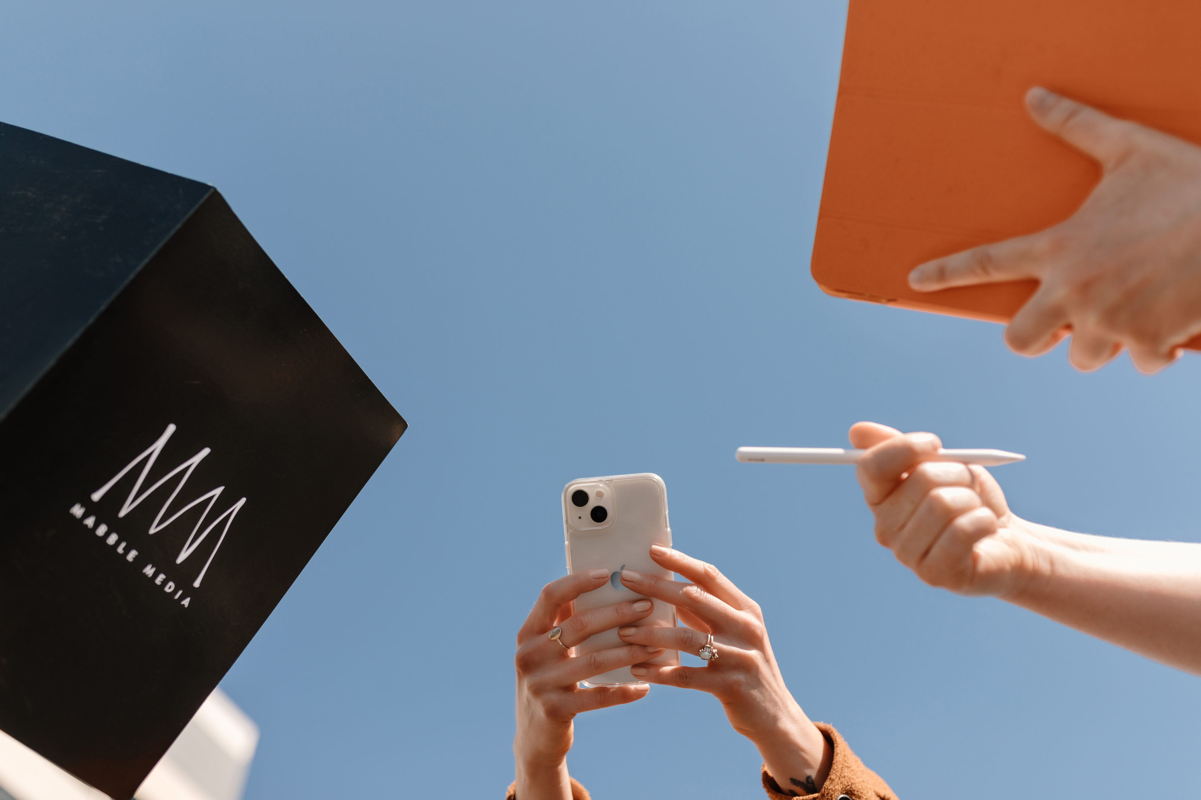 three people holding a phone and ipad and a notebook with mabbles logo