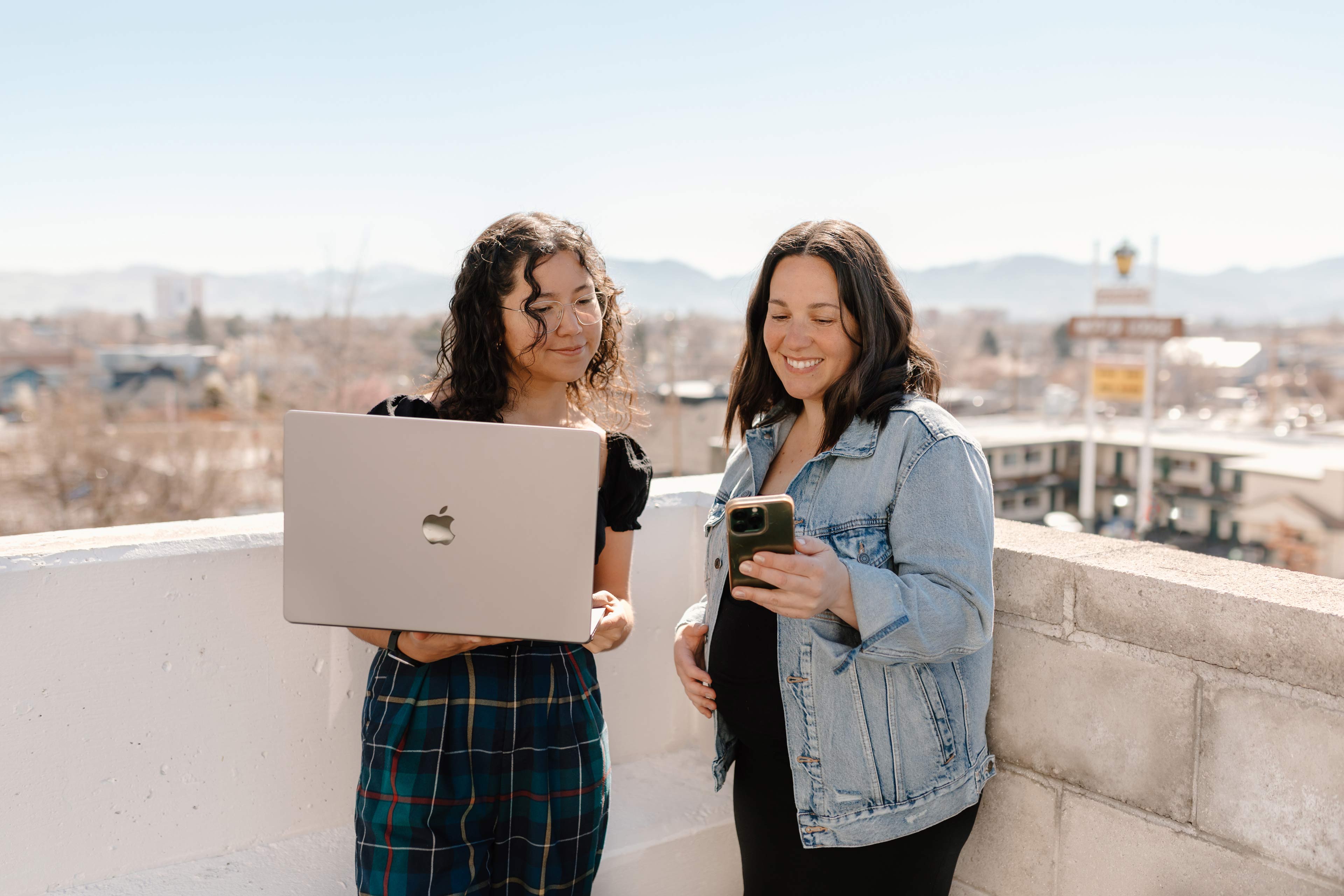 two women looking at a laptop and phone